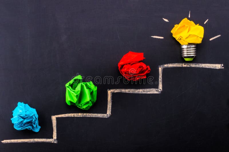 Evolving idea concept with colorful crumpled paper and light bulb on steps drawn on blackboard stock photo Evolving idea concept with colorful crumpled paper and light bulb on steps drawn on blackboard stock photo