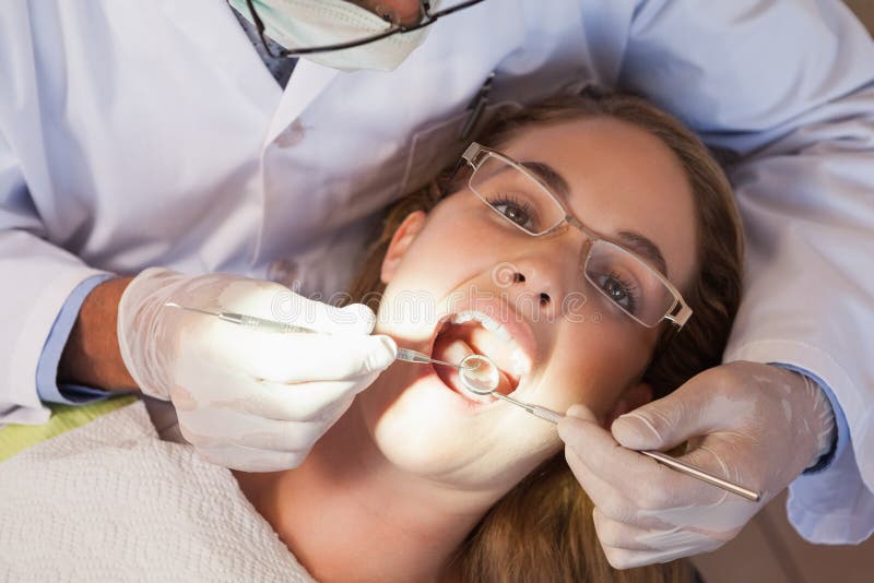 Dentist examining a patients teeth in the dentists chair under bright light at the dental clinic. Dentist examining a patients teeth in the dentists chair under bright light at the dental clinic