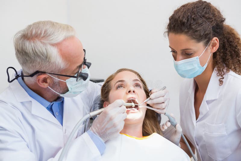 Dentist examining a patients teeth in the dentists chair with assistant at the dental clinic. Dentist examining a patients teeth in the dentists chair with assistant at the dental clinic