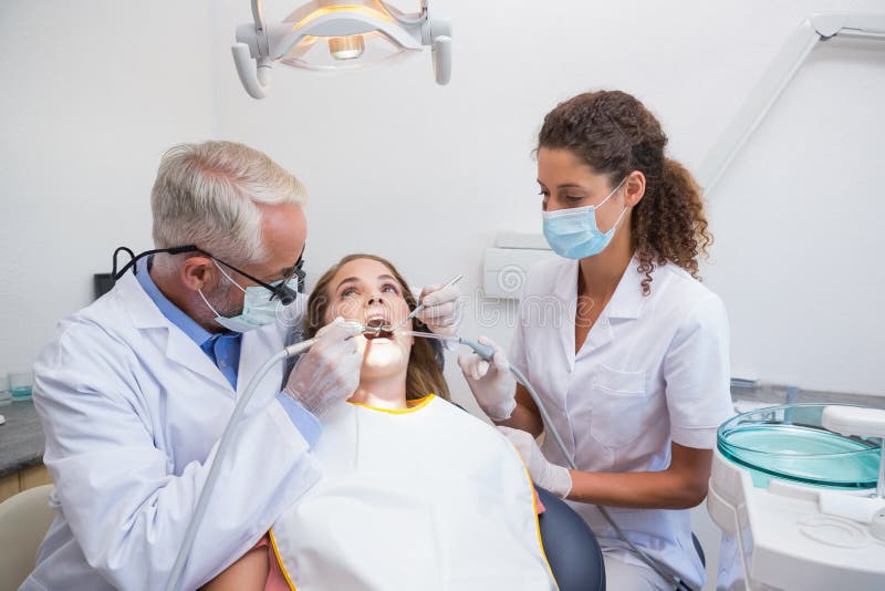 Dentist examining a patients teeth in the dentists chair with assistant at the dental clinic. Dentist examining a patients teeth in the dentists chair with assistant at the dental clinic