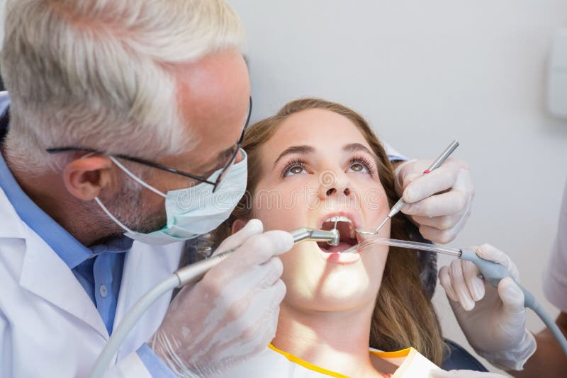 Dentist examining a patients teeth in the dentists chair with assistant at the dental clinic. Dentist examining a patients teeth in the dentists chair with assistant at the dental clinic