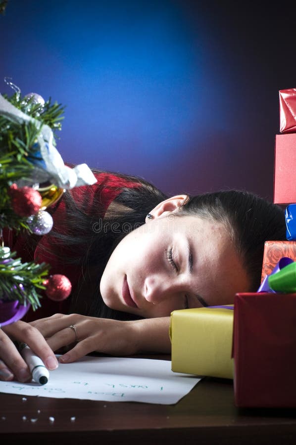 A view of a teenage girl sleeping with her head on a desk or table, surrounded with Christmas presents and a small tree. A view of a teenage girl sleeping with her head on a desk or table, surrounded with Christmas presents and a small tree.