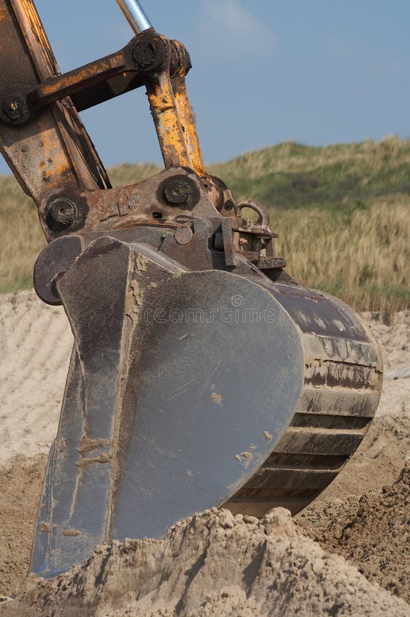 The steel teeth/mouth of an earth moving machine/digger. Digging in sand with blue background sky. The steel teeth/mouth of an earth moving machine/digger. Digging in sand with blue background sky.