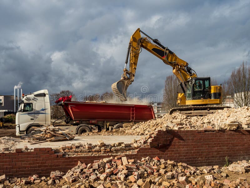 An Excavator Breaks Down An Old Building. Dust, Bricks And Broken Walls