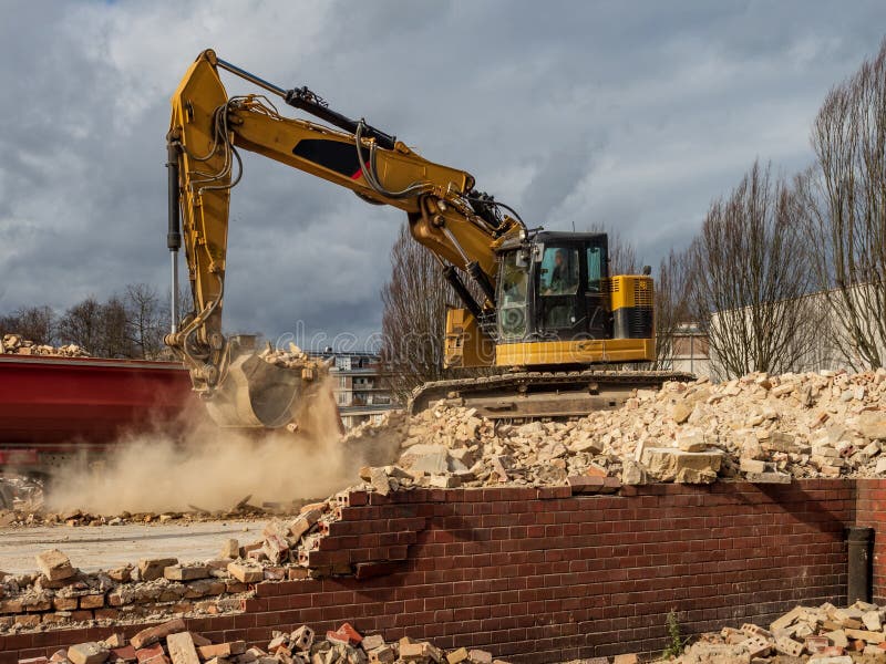 An excavator breaks down an old building. Dust, bricks and broken walls.