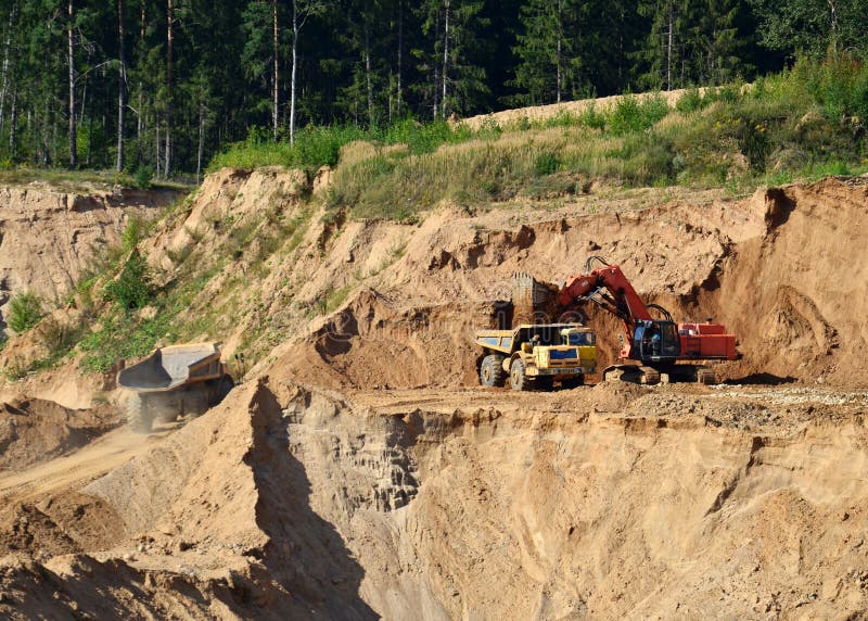 Excavator load the sand to the heavy mining truck in the open-pit. Heavy machinery working in the mining quarry. Digging and royalty free stock photography