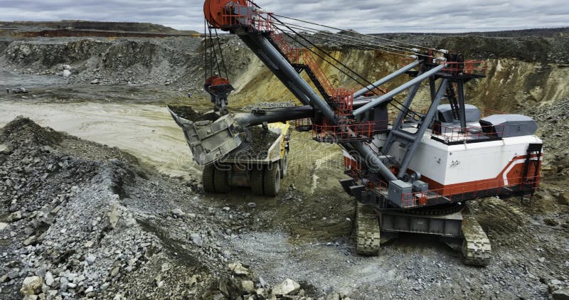 Heavy excavator loading dump truck in open-pit mining quarry