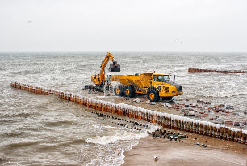 Excavator loading a truck stones on the beach