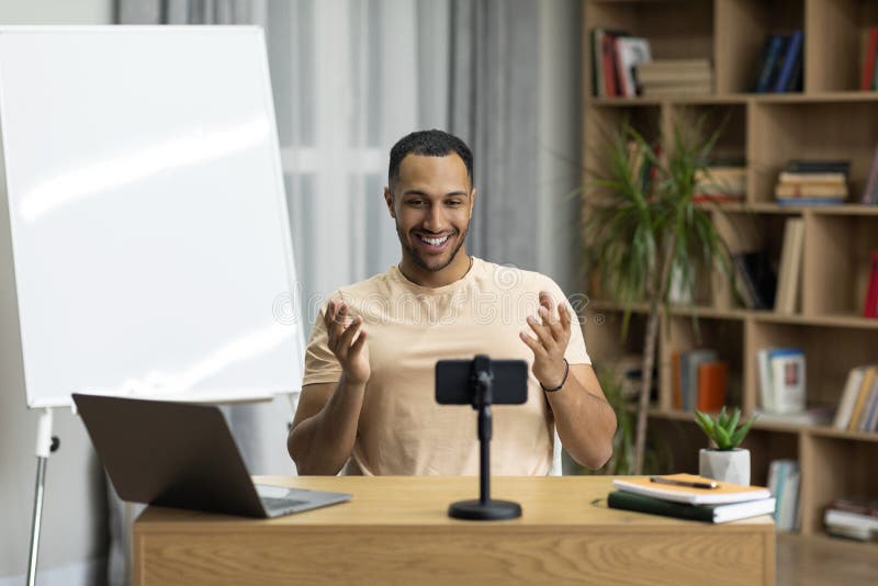 Excited arab man sitting in front of smartphone, recording video or having live videoconference with students stock photos