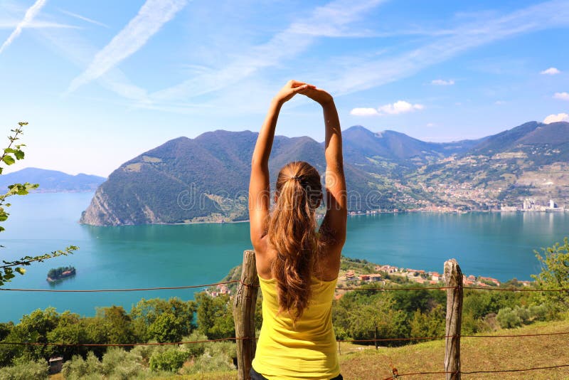 Excited attractive young woman in sportswear stretching enjoying Lake Iseo landscape in the morning, North Italy. Cheerful mood