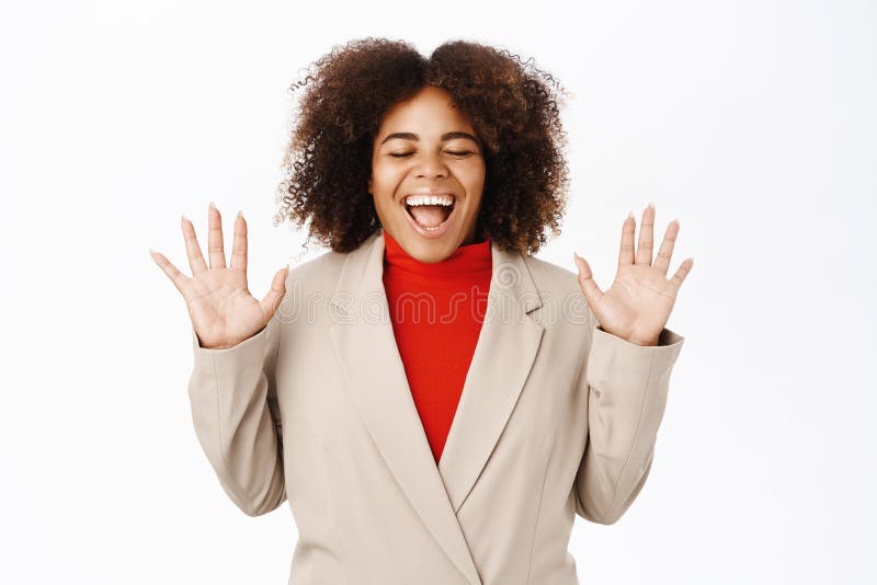 Excited Black woman screams of joy, wears suit, celebrates and triumphs, stands over white background