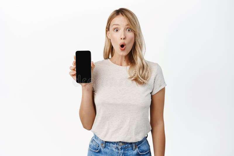 Excited blond girl showing mobile phone screen, say wow, demonstrating smartphone app interface, standing over white