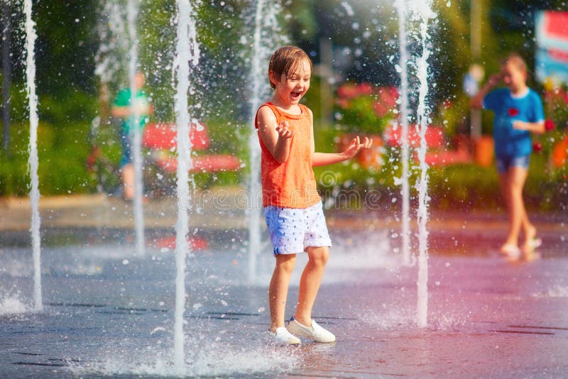 Excited boy having fun between water jets, in fountain. Summer in the city