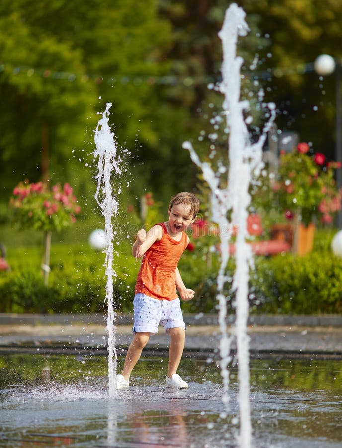 Excited boy having fun between water jets, in fountain. Summer in the city