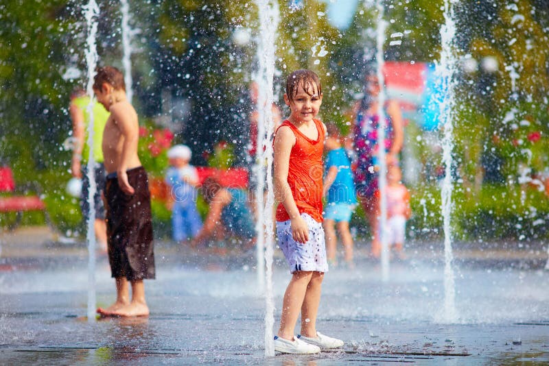 Excited boy having fun between water jets, in fountain. Summer i
