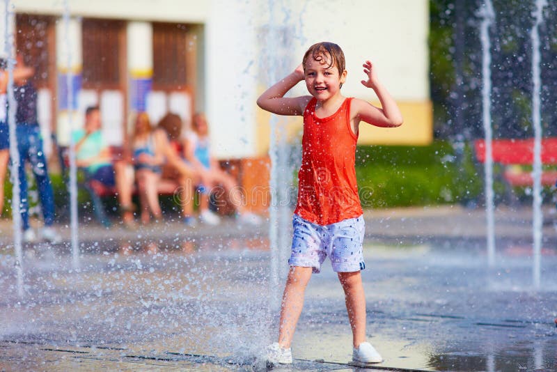 Excited boy having fun between water jets, in fountain. Summer i