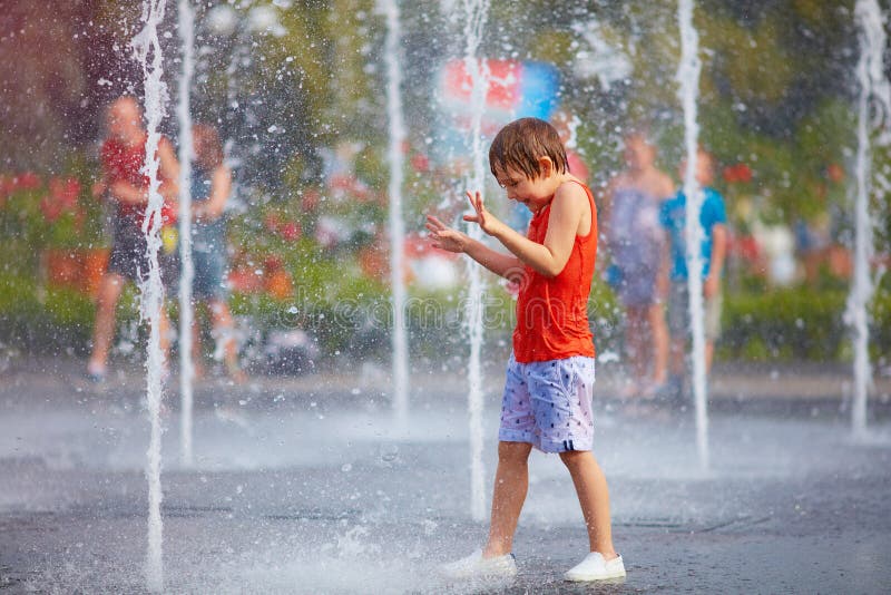 Excited boy having fun between water splashes, in fountain. Summer in the city