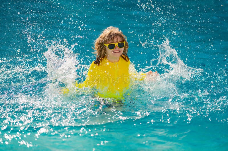 Excited child splashing water in pool. Little kid splashing in blue water of swimming pool. Cute boy swimming and royalty free stock image