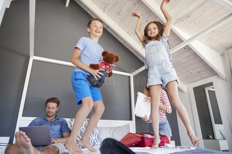 Excited Children Jump on Bed As Parents Pack for Vacation Stock Image Image of children