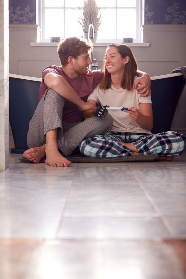 Excited Couple With Woman With Prosthetic Arm Sitting On Bathroom Floor With Positive Pregnancy