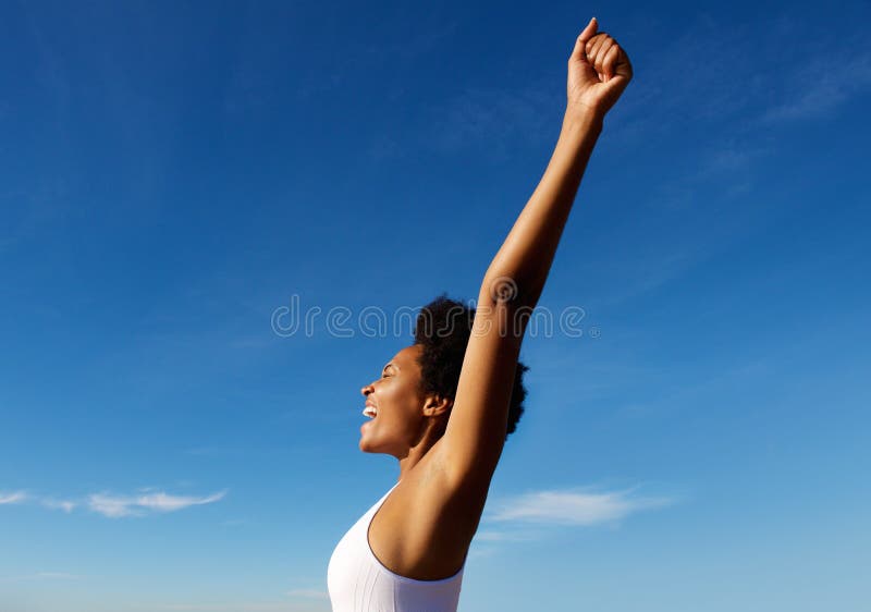 Side view portrait of excited fitness woman standing outdoors against blue sky with her hands raised. Side view portrait of excited fitness woman standing outdoors against blue sky with her hands raised