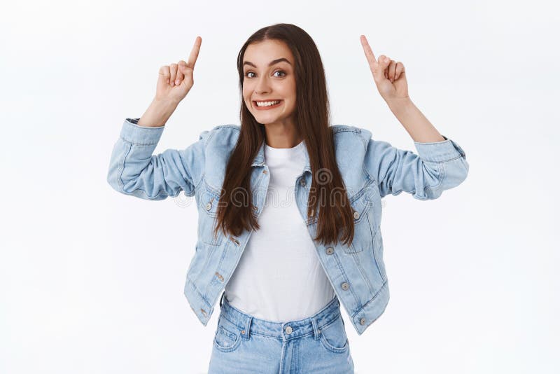 Excited, funny and pretty brunette caucasian female in denim jacket, jeans, pointing fingers up smiling cheerful