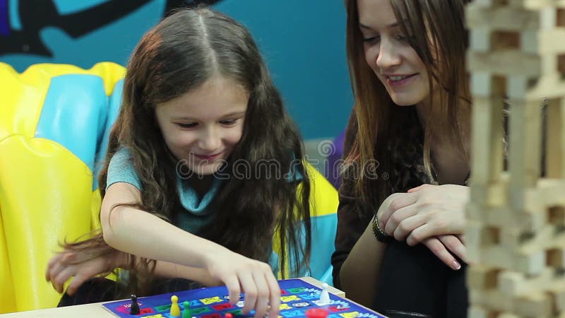 Excited girl chats woman, plays board game, educational process