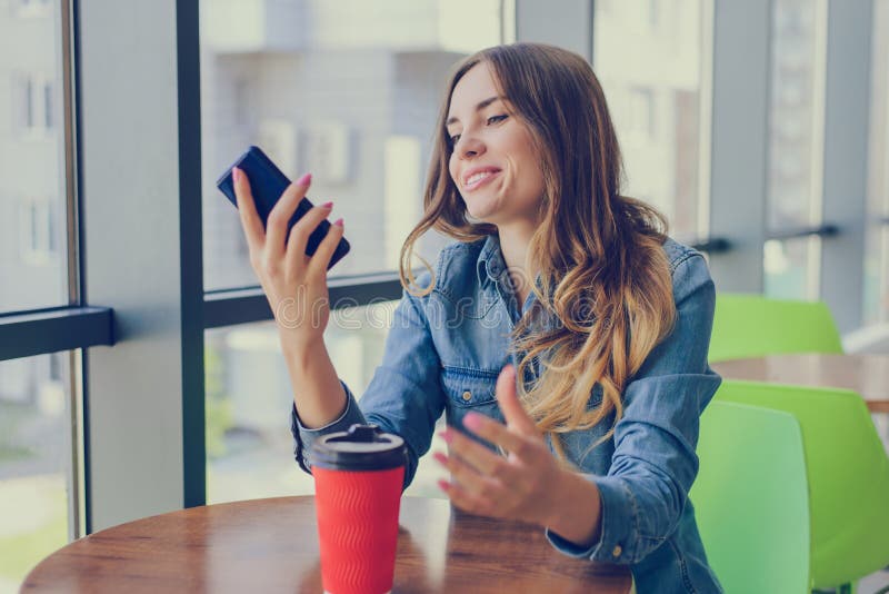 Excited smiling happy woman having a rest in a cafe, she is looking at screen of her smartphone telephone mobile phone sms notific