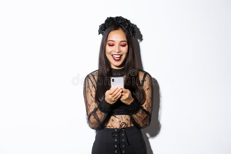 Excited smiling woman looking at mobile phone pleased, wearing gothic lace dress for halloween party, standing over