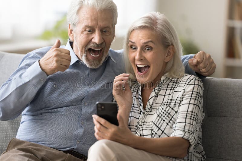 Excited surprised retired couple holding mobile phone