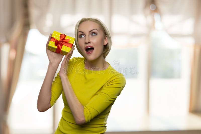 Excited woman with opened mouth holding a small gift box.