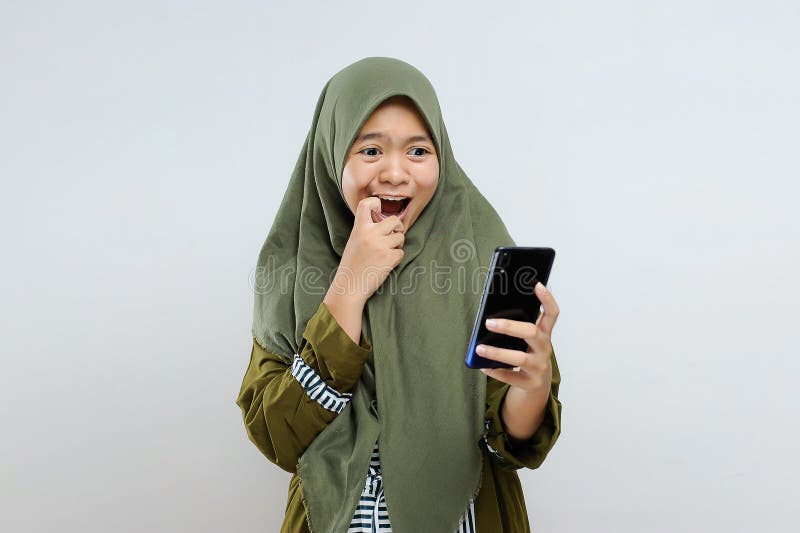 Excited young Asian Muslim woman shock look at smartphone get best gift / voucher / discount