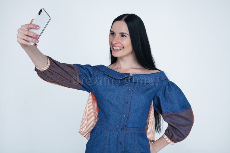 Excited young brunette woman making selfie using smart phone. Student girl with long hair in jeans shirt taking photograph with royalty free stock photography Excited young brunette woman making selfie using smart phone. Student girl with long hair in jeans shirt taking photograph with royalty free stock photography