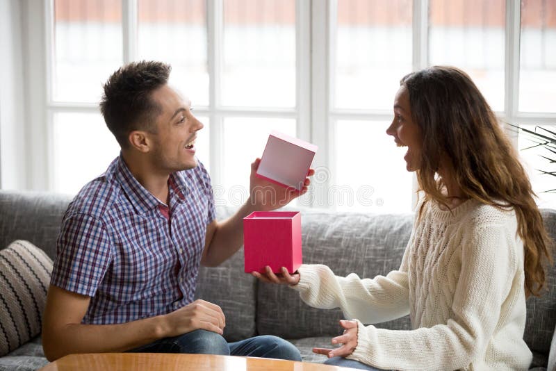 Excited young man opening gift box receiving present from wife