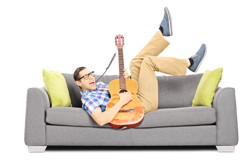 Excited young male lying on a sofa and playing a guitar