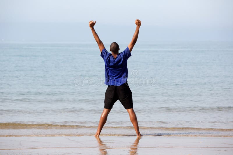Excited young man standing on beach with arms outstretched. Rear view full body portrait of excited young man standing on beach with arms outstretched stock images Excited young man standing on beach with arms outstretched. Rear view full body portrait of excited young man standing on beach with arms outstretched stock images