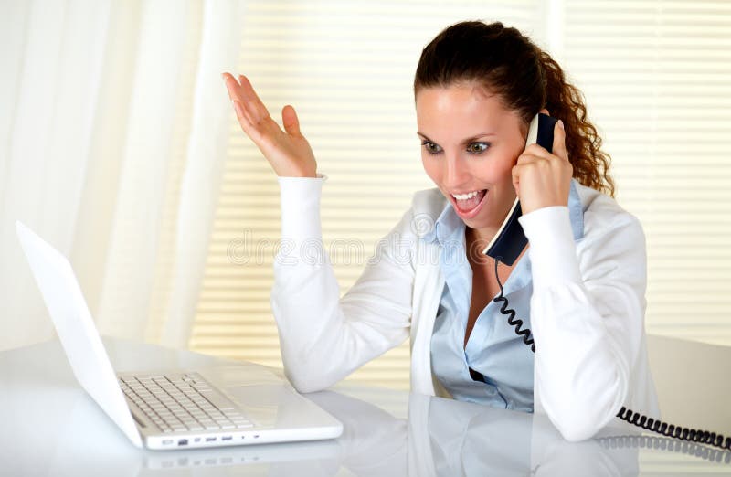 Excited young woman talking on phone in front of her laptop