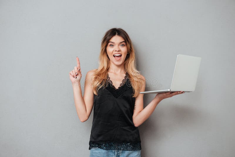 Excited девушка держа компьтер-книжку и указывая палец вверх на copyspace стоковые фотографии rf