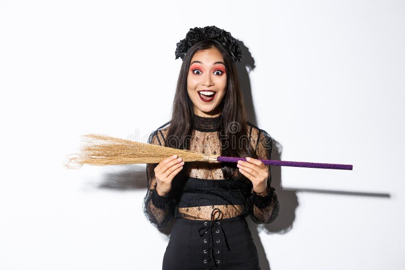 Excited young asian girl in witch costume looking amazed, showing small broom, standing over white background. Excited young asian girl in witch costume looking amazed, showing small broom, standing over white background.