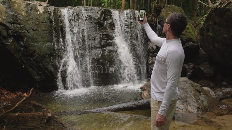 Excursionista grabando un vídeo de una cascada en el bosque