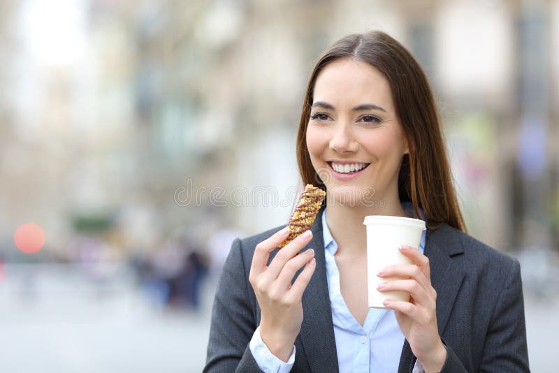 Executive holding snack bar and takeaway coffee in the street