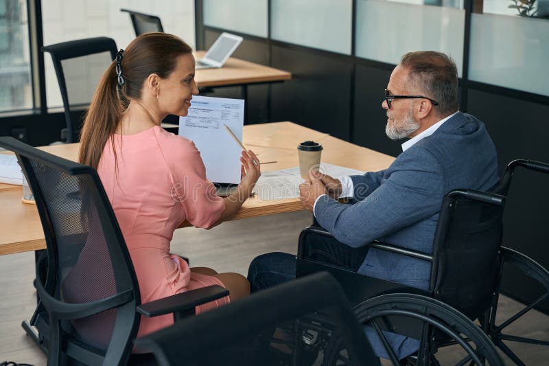 Executive in Wheelchair and Employee Work at the Office Table Stock