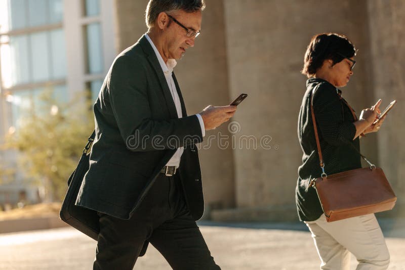 Executivos do telefone celular de utilização ocupado ao andar na rua fotos de stock royalty free Executivos do telefone celular de utilização ocupado ao andar na rua fotos de stock royalty free