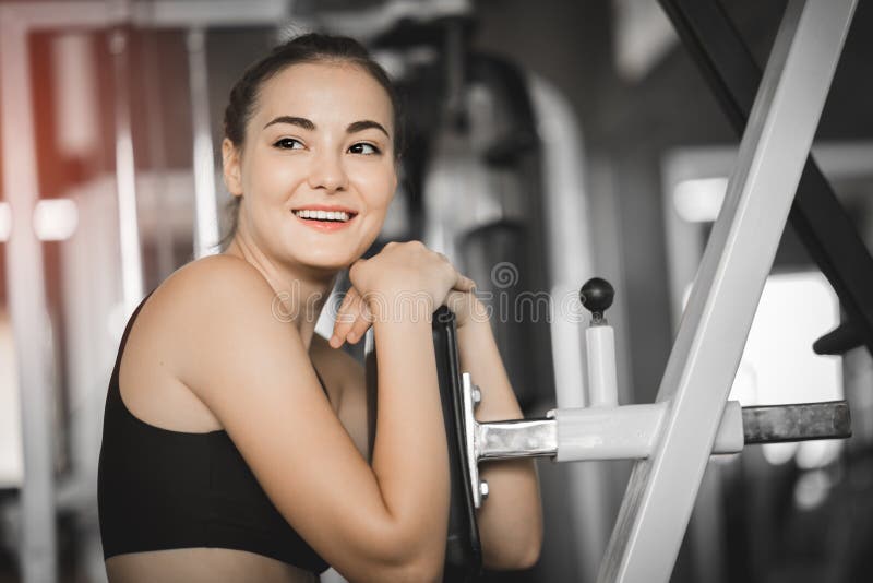 Exercício bonito apto do exercício da jovem mulher na máquina no gym A menina de sorriso contente deve apreciar com seu processo