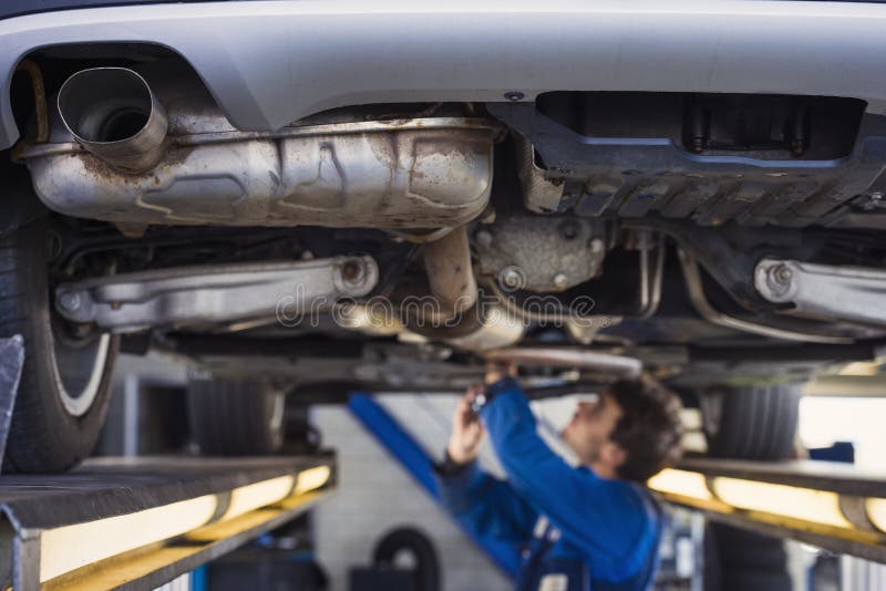 Exhaust of a car with mechanic underneath. Exhaust of a car on the bridge at a auto repair shop with a mechanic underneath stock photo Exhaust of a car with mechanic underneath. Exhaust of a car on the bridge at a auto repair shop with a mechanic underneath stock photo