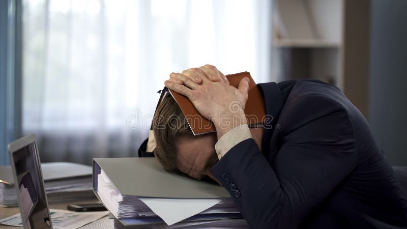 Exhausted businessman putting notebook on head at workplace, deadline pressure royalty free stock image Exhausted businessman putting notebook on head at workplace, deadline pressure royalty free stock image