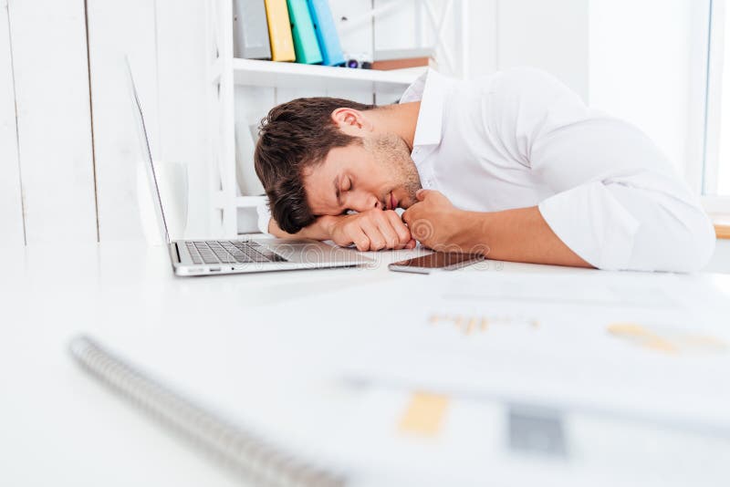 Exhausted fatigued young businessman sleeping on the table in office