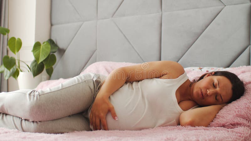 Expectant mother suffering from pregnant pain. Pregnant woman feeling ache lying on a bad.  Pregnant adult woman feels pain