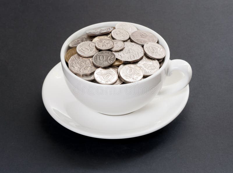 Expensive coffee. White cup filled with Australian coins, on a white saucer against a black textured background. All coins are front side up royalty free stock photo Expensive coffee. White cup filled with Australian coins, on a white saucer against a black textured background. All coins are front side up royalty free stock photo