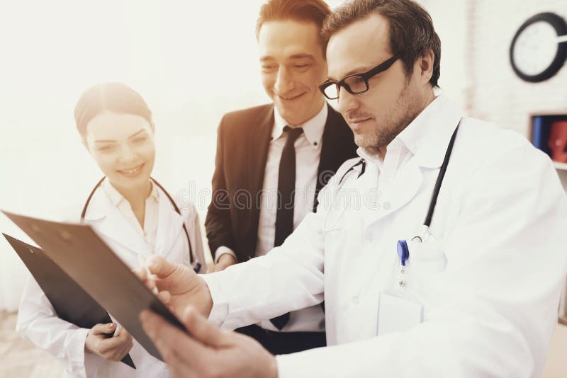 Experienced doctor with nurse shows results of analyzes to smiling businessman in office. stock photo Experienced doctor with nurse shows results of analyzes to smiling businessman in office. stock photo